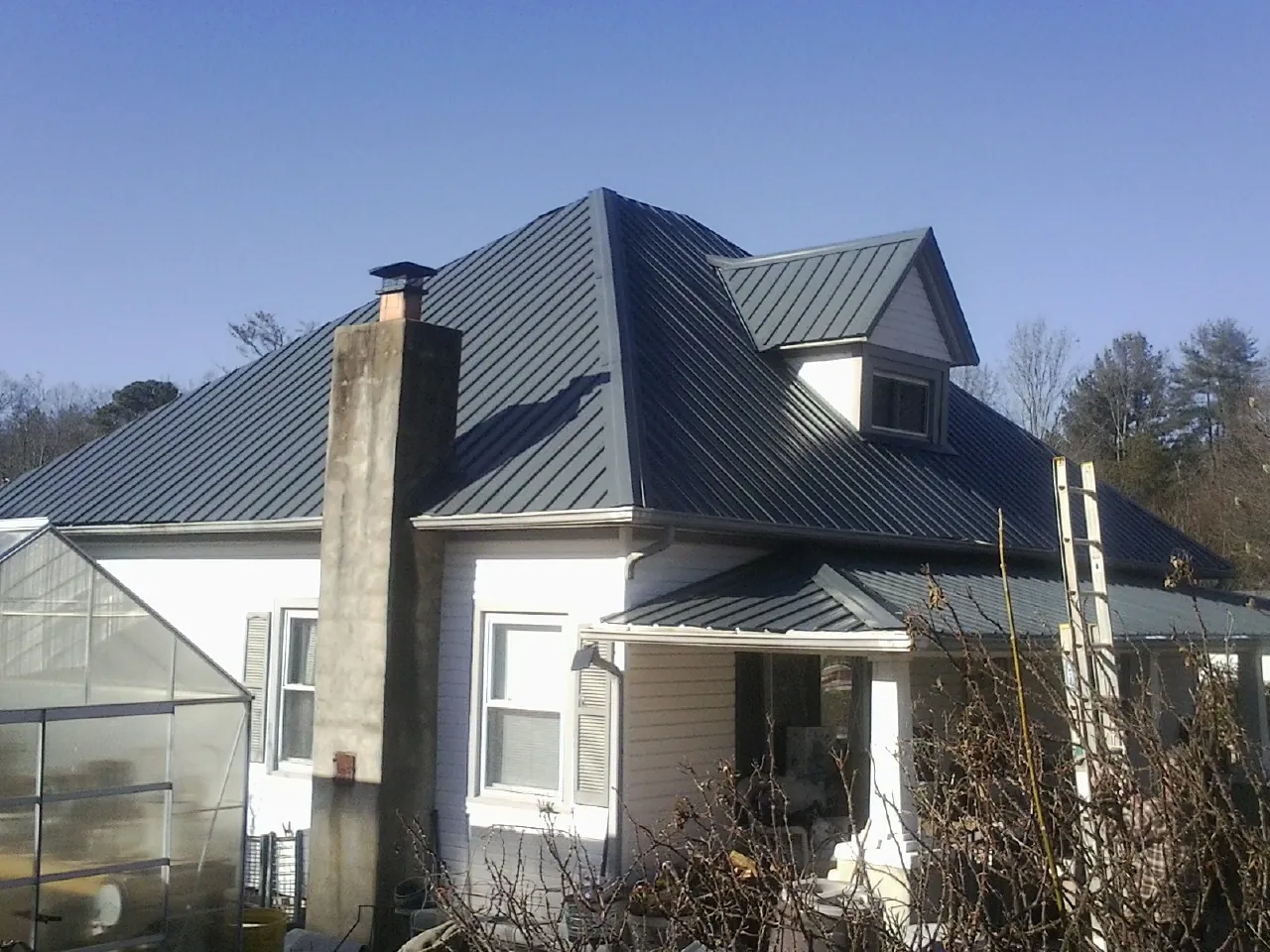 Dark blue standing seam metal roof on a white farmhouse with dormer — Slate & Tile Roof Repair by Roofing Brothers in Ramer