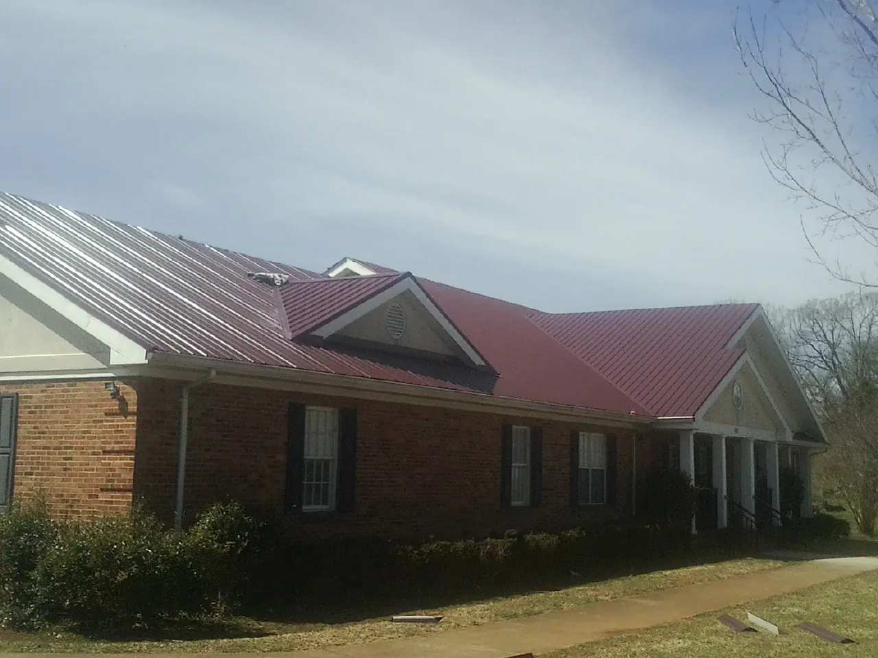 Red metal roof with gabled entries on a long brick building, from a Hail Damage Roof Repair job in Ramer
