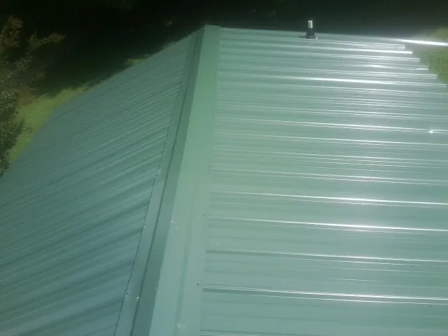 New green metal panels meeting at the ridge of a roof — Flat Roof Repair work by our crew in Ramer