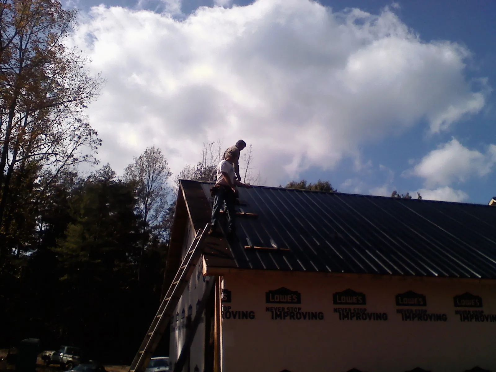 Roofer fastening dark metal panels high against a cloudy sky, from a Roof Inspection job in Ramer